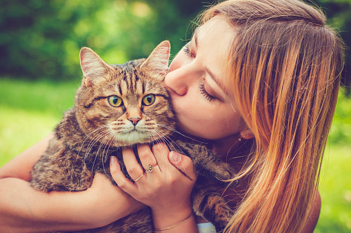 Happy young woman and her cat outdoors in a park in summer