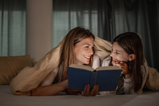 Young woman and her cute daughter reading a book together before sleep stock photo