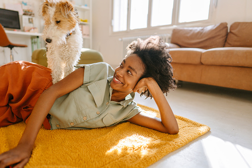 Young woman and her dog enjoying together rays of sunshine in a living room
