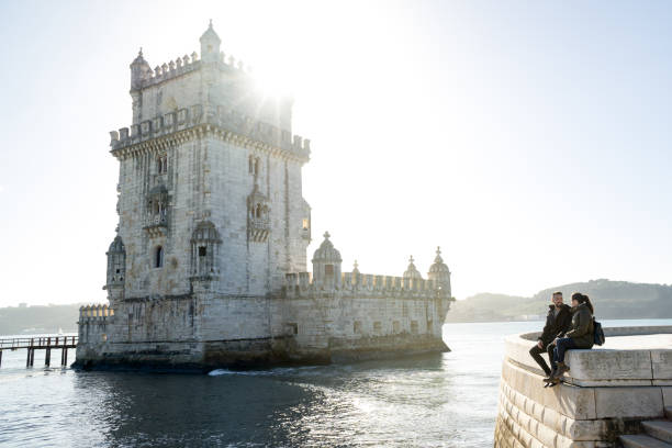 young woman and man sitting next to the belem tower in lisbon. - castle couple stockfoto's en -beelden