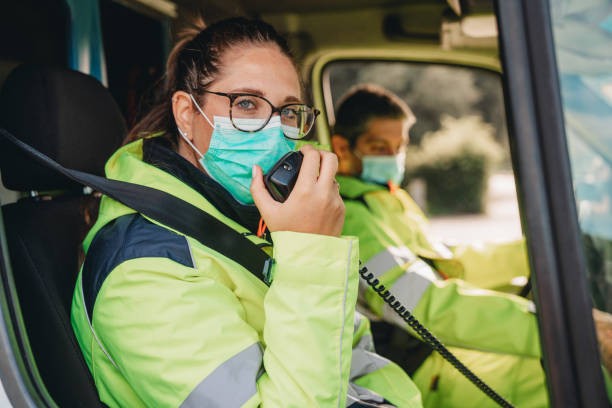 Young woman answering a call in an ambulance Young woman answering a call in an ambulance. She's with her colleague. They are wearing protective face masks. audio electronics stock pictures, royalty-free photos & images