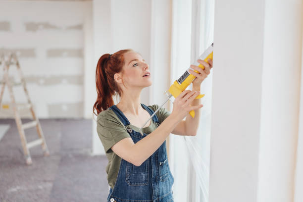 Young woman applying glue from a gun Young woman applying glue from a gun to a window frame during home renovations in an unfinished living room diy stock pictures, royalty-free photos & images