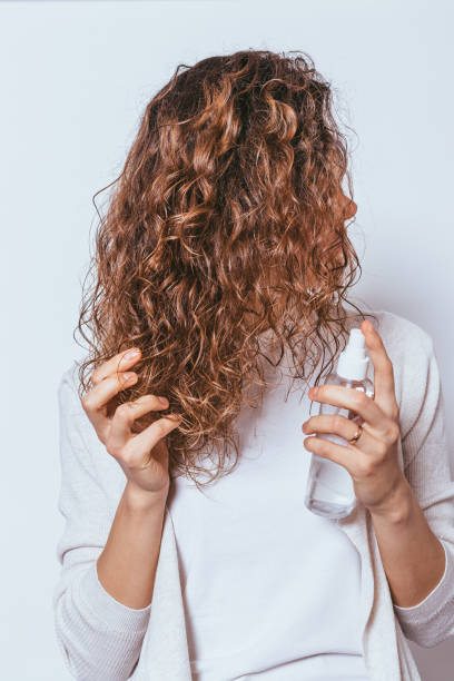 Young woman applying moisturizing spray to her curly hair stock photo