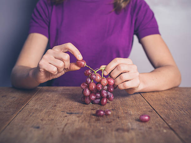 Young woman at table eating grapes stock photo