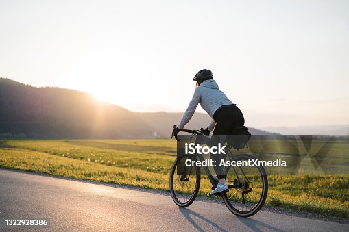 istock Young woman bikes down country road at sunrise 1322928386