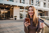 Happy young woman with mobile phone is buying online with her credit card and smart phone outdoors