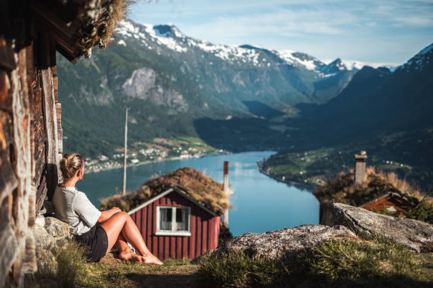 Woman relaxing by fjord and cabins by Lovatnet/Raksetra, Norway.
