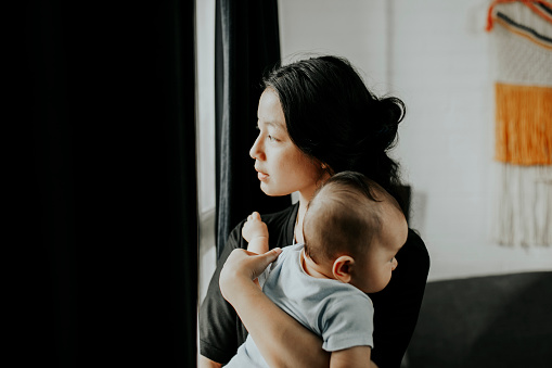 Young woman carrying baby looking throughout window