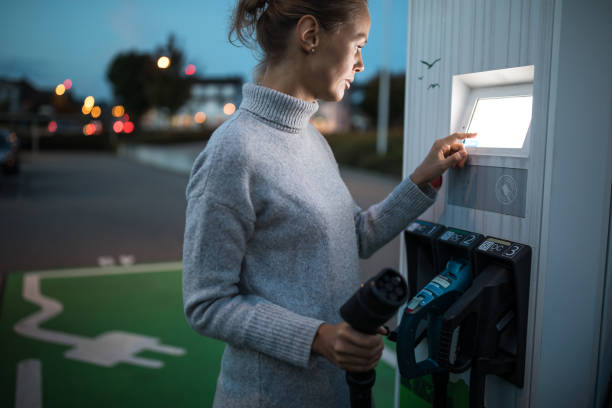 young woman charging an electric vehicle - car charger imagens e fotografias de stock