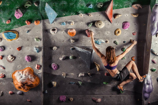 Young woman climbing up on practice wall Young woman climbing up on practice wall in gym bouldering stock pictures, royalty-free photos & images
