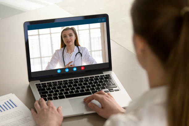 Young woman consulting with family therapist online via video call. Shoulder view young woman consulting with family therapist doctor general practitioner online via video call on laptop after feeling first virus illness symptoms, medical insurance, covid19 outspread. nurse talking to camera stock pictures, royalty-free photos & images