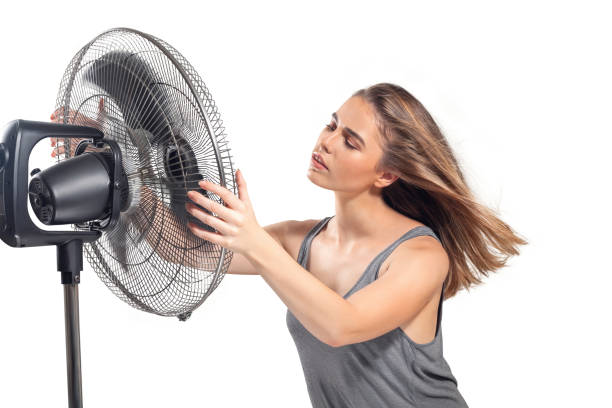 Young woman cooling down with electric fan stock photo