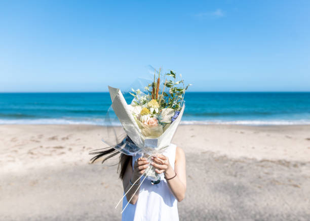 ビーチで花束で顔を覆う若い女性 - 花束 ストックフォトと画像