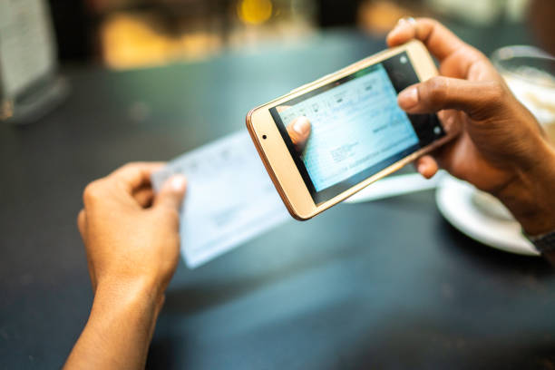 jonge vrouw deponeren check per telefoon in het cafe - draagbare informatie apparatuur stockfoto's en -beelden