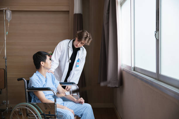Young woman doctor explaining information to man patient in wheelchair in medical face mask while talking together in hospital. Epidemic and virus concept Young woman doctor explaining information to man patient in wheelchair in medical face mask while talking together in hospital. Epidemic and virus concept physical therapy programs stock pictures, royalty-free photos & images