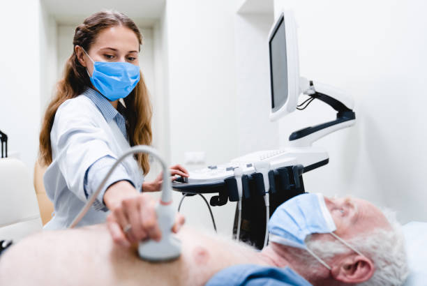 junge ärztin in maske überprüft ältere patienten brust mit ultraschallgeräten - diagnosehilfe stock-fotos und bilder