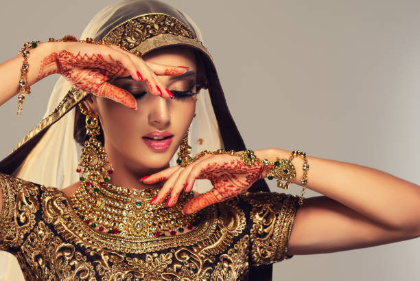Young woman dressed in posh, gilded, Indian costume, Kundan style jewelry and henna tattoo(mehndi) on the hands. Traditional Indian costume lehenga choli. National Indian style. stock photo