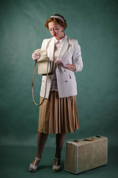A young woman, dressed in retro style, with a suitcase at her feet, examines the contents of her purse stock photo