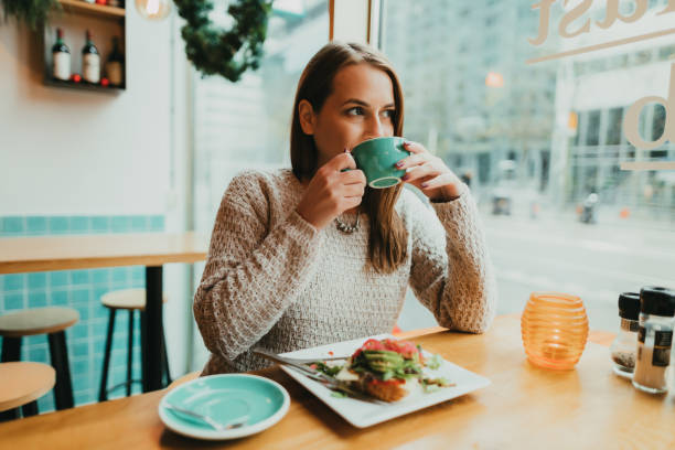 Young woman drinking coffee and eating avocado toast for breakfast stock photo