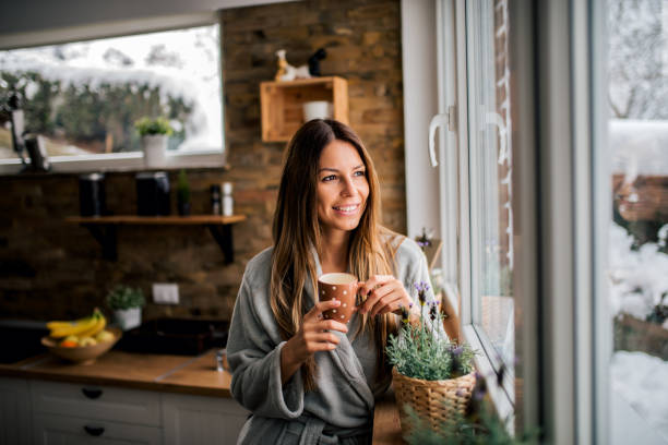 jonge vrouw het drinken van koffie in de ochtend, kijkend naar venster. - woman drinking coffee stockfoto's en -beelden