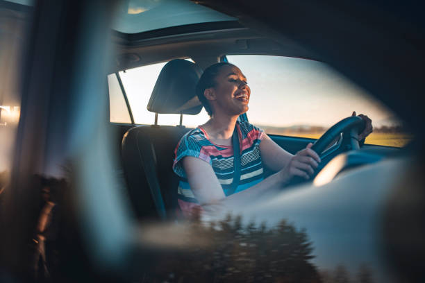 Young woman driving car on a sunny day Young African-American woman in a car. She is driving, smiling and looking out. She is singing and having fun on a sunny spring afternoon. singing stock pictures, royalty-free photos & images