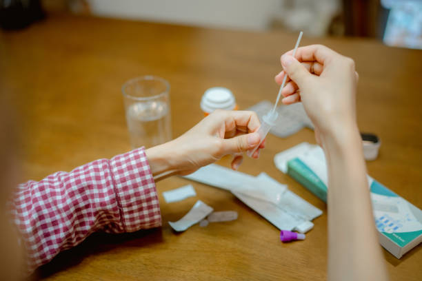 Young woman drops swab in a protective plastic tube. Asian woman drops swab in a protective plastic tube after nasal swab test to check for virus at home. at home covid test stock pictures, royalty-free photos & images