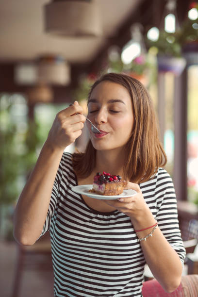 молодая женщина ест вкусный десерт в городском кафе - готовый к употреблению стоковые фото и изображения