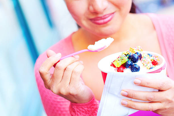 Young woman eating frozen yogurt topped with assorted sweets stock photo