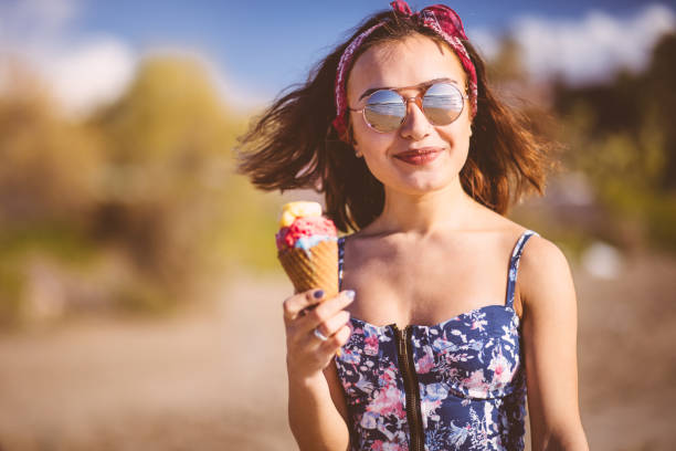Young woman eating ice cream on the beach Young brunette woman in boho style eating ice cream at the beach hot latino girl stock pictures, royalty-free photos & images