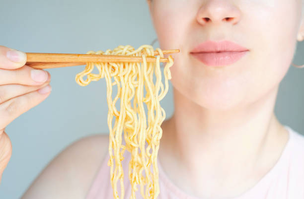 Young woman eating instant ramen noodles close-up on gray background. stock photo