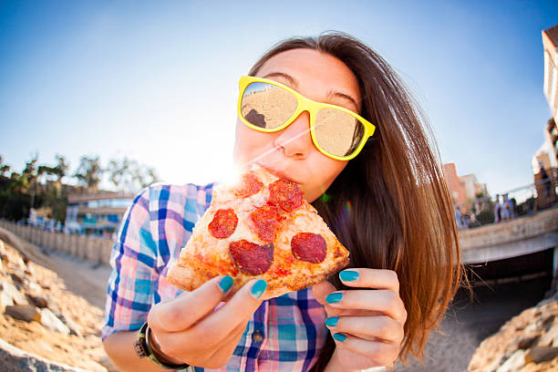 Young Woman Eating Pizza Close-up Of A Happy Young Woman Wearing Sunglasses Eating Pizza fish eye lens stock pictures, royalty-free photos & images