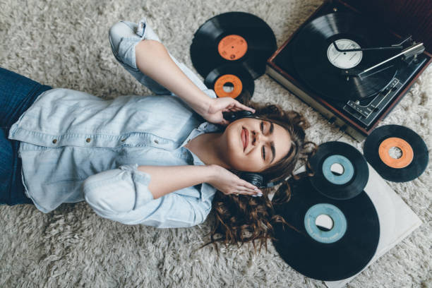 Young woman enjoing music from gramophone Young retro woman listening music on floor turntable stock pictures, royalty-free photos & images