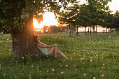 Young woman enjoying sunset under tree, thinking about future, relaxing, feeling free.