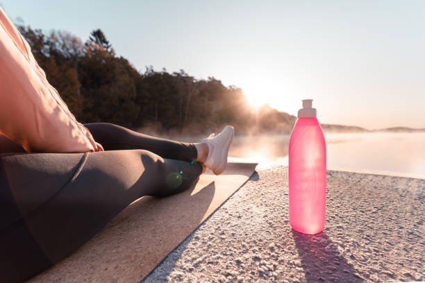 Young woman exercising yoga in the early morning A young woman is exercising yoga by a lake early in the morning on a beautiful autumn day. She is leaning back, enjoying the sun. reusable water bottle stock pictures, royalty-free photos & images