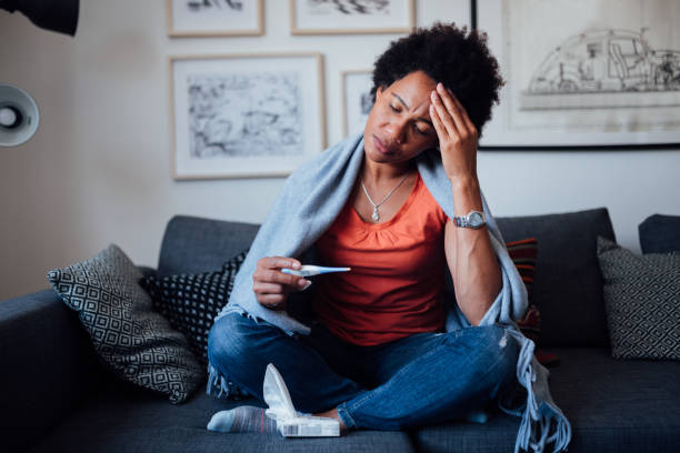 Young woman feeling symptoms of an illness Worried African American woman sitting at home while being sick fever stock pictures, royalty-free photos & images