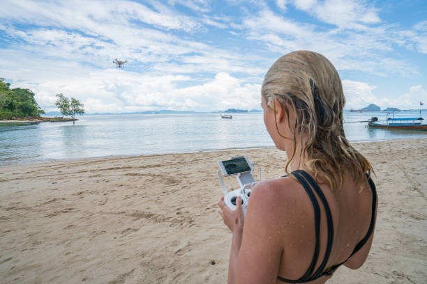 jovem mulher sobrevoando um drone numa praia tropical na tailândia. - drone sobrevoando o mar - fotografias e filmes do acervo