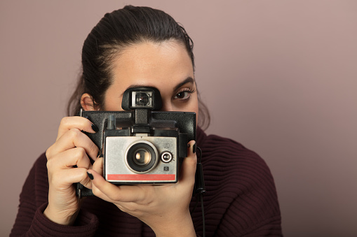 Young woman focusing on the viewer and taking picture with a vintage camera