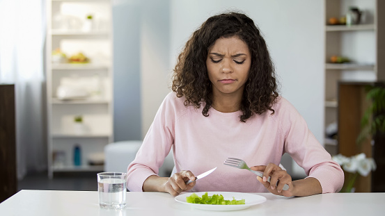 Young woman forcing herself to eat salad, dissatisfaction, weight. 