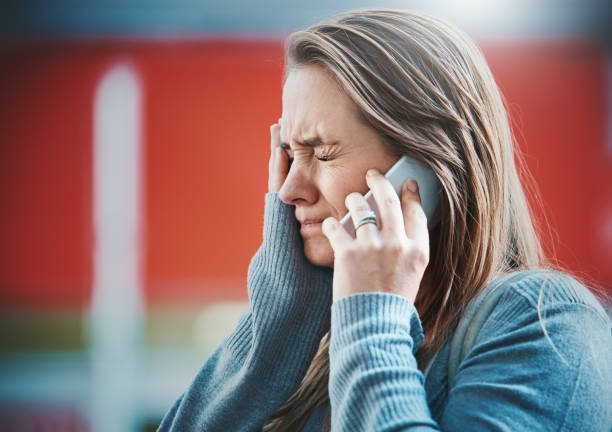Young woman gets bad news on her mobile phone A young blonde woman grimaces, hand to her face as she hears something on her smart phone, obviously bad news. bad news stock pictures, royalty-free photos & images