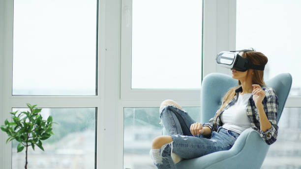 Young woman have VR experience using virtual reality headset sitting in chair on balcony stock photo