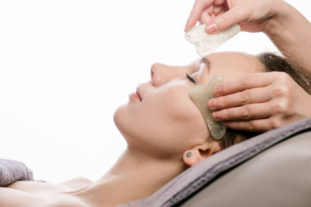 Young woman having a gua sha face massage at asian beauty clinic. Side view stock photo