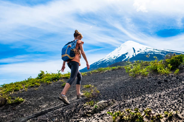 Young woman hiker walks on the loose rocky trail with snow capped volcano on the background. Trekking to volcano of Osorno in Chile stock photo