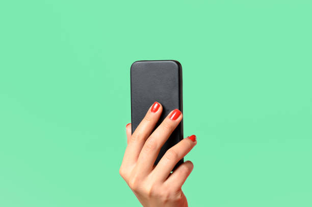 Young woman holding a mobile phone Young woman with red painted fingernails holding a mobile phone in the air with the back towards the camera, close up isolated on green smart phone green background stock pictures, royalty-free photos & images