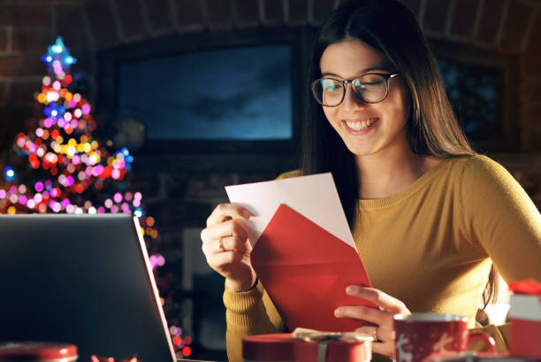 jonge vrouw die een envelop met een kaart van kerstmis houdt - kerstkaart stockfoto's en -beelden