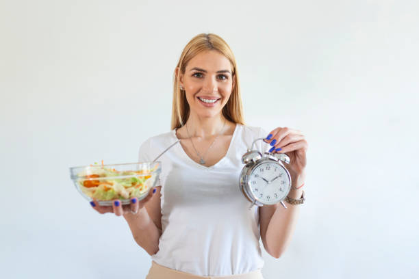 Young woman holding clock and Healthy food of salad Intermittent fasting concept. Time to lose weight , eating control or time to diet concept. stock photo