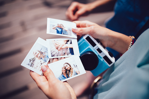 Young woman holding polaroid photos with mum on summer holidays