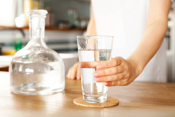 若い女性はコップ一杯の水を持っています。あなたの手のクローズアップで透明なガラスの中できれいな飲料水。 ストックフォト