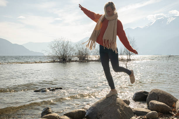Young woman hops from rock to rock by the lakeshore stock photo