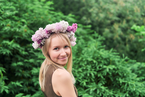 young woman in a floral wreath of lilac flowers on a natural background outdoors