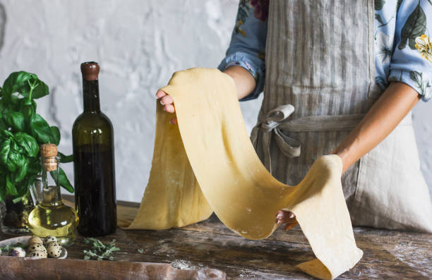 Young woman in apron holding the dough for homemade pasta at rustic kitchen stock photo